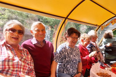 Gruppenbild der linken Sitzbank mit fünf Personen, die teils in die Kamera lächeln.