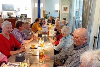 Bild zeigt eine lange Tafel mit Personen an den Tischen