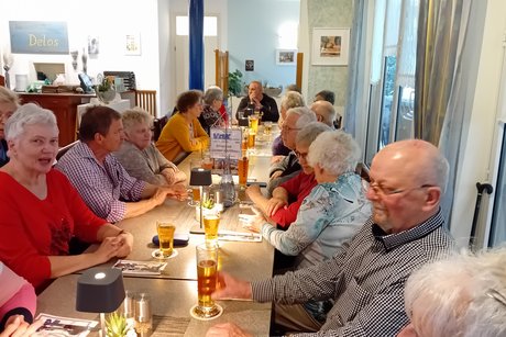 Bild zeigt eine lange Tafel mit Personen an den Tischen