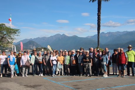 Alle Reiseteilnehmer stehen an der Promenade von Stresa im Hintergrund die Berge bei leicht bewölktem Himmel
