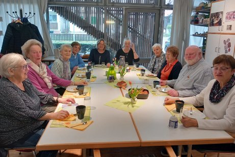 Neun Frauen und ein Mann bei einer geselligen Runde an einem gedeckten Tisch mit Kaffee und Kuchen.