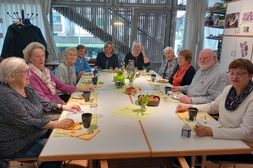 Neun Frauen und ein Mann bei einer geselligen Runde an einem gedeckten Tisch mit Kaffee und Kuchen.