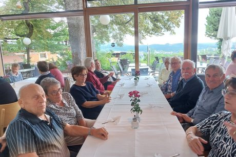 Sommerausflug VdK OV RSKN-Esslingen 2025 Ältere Menschen an einem langen Tisch mit weißem Tischtuch, teils in die Kamera blickend, während sie sich unterhalten