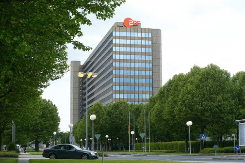 Das ZDF Hochhausgebäude des ZDF mit Logo oben, im Vordergrund Bäume und Straße mit 1 Pkw