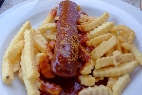 Das Bild zeigt eine Currywurst mit Pommes