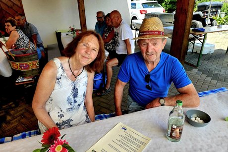 Eine Frau im hellen Kleid und ein Mann im blauen Hemd und einem Strohhut l&auml;cheln in die Kamera