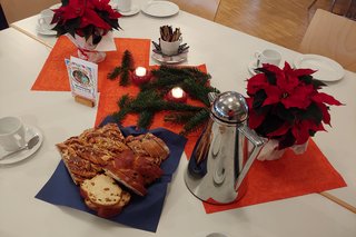 Gedeckter Tisch mit Kerzen, Geschirr, Rosinenzopf und Weihnachtsstern