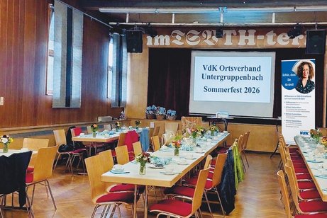 Saal mit geschm&uuml;ckten Tischreihen. Hintergrund B&uuml;hne mit gro&szlig;er Leinwand. Text: VdK Ortsverband Untergruppenbach Sommerfest 2026