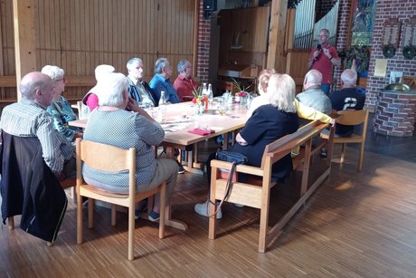 Menschen sitzen an Tischen und hören einem Vortrag zu.