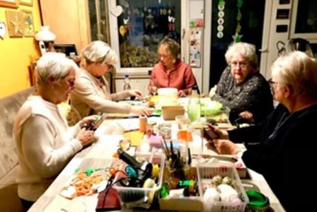 Bastel- und Dekogruppe: mehrere Frauen sitzen an einem voll beladenen Tisch mit bunten Bastelutensilien und fertigen Basteleien zu Ostern