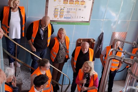 Die Teilnehmenden hören interessiert der Brauereiführung zu. Sie stehen vor einem großen Braukessel und tragen Warnwesten.