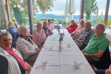 Sommerausflug VdK OV RSKN-Esslingen 2025 Ältere Menschen an einem langen Tisch mit weißem Tischtuch, teils in die Kamera blickend, während sie sich unterhalten