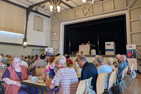 Panorama vom Festsaal. Zentral eine Tischreihe, an der mehrere ältere Menschen sitzen, Kuchen essen und Kaffee trinken.