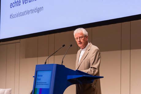 Werner Raab steht am Pult und Mikrofon und spricht