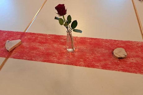 Tisch mit rotem Tischband, einzelner Rose in einer kleinen Flasche und 2 kleinen Holzscheiben