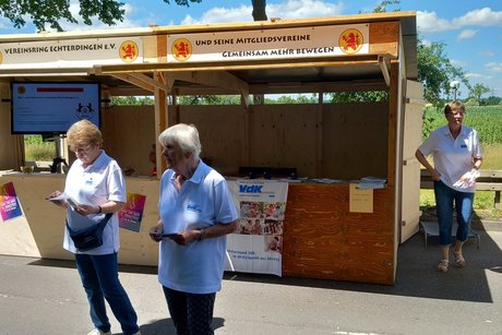 Zwei Frauen mit VdK-Poloshirts vor einem Holzstand, sie halten VdK-Broschüren in den Händen.