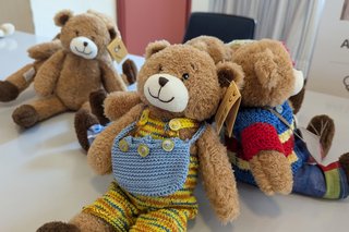 Teddybär, eingekleidet in eine gestrickte Latzhose und mit einer gestrickten Umhängetasche.