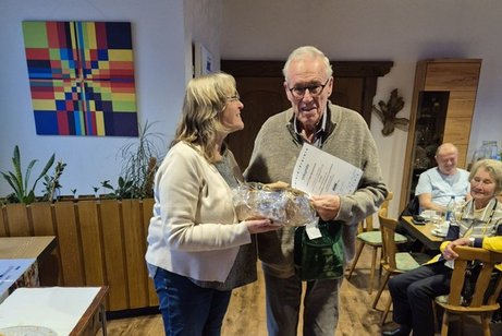 Eine Frau &uuml;berreicht einem &auml;lteren Mann eine Urkunde und ein Geschenk.Eine Frau &uuml;berreicht einem &auml;lteren Mann eine Urkunde und ein Geschenk.