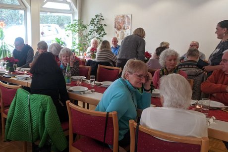 Panoramafoto des Festsaals mit mehreren Tischen, an denen vorwiegend &auml;ltere Menschen sitzen und sich angeregt unterhalten