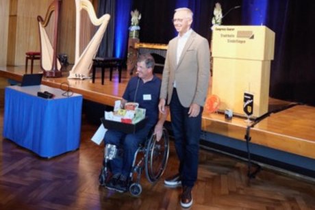 Auf der B&uuml;hne eines gro&szlig;en Saals steht Christian Gangl, der erste B&uuml;rgermeister von Sindelfingen, neben Roger Hahn, dem Vorsitzenden des VdK Ortsverbands Sindelfingen, der in einem Rollstuhl sitzt. Im Hintergrund sind zwei Harfen und ein Rednerpult zu erkennen.