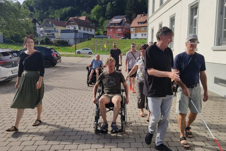 Die VdK-Ortsvorsitzende Verena Diemer schreitet neben dem im Rollstuhl sitzenden Stadtrat Klaus Eckert her, Stadtrat Bernhard "Pi" Steinebrunner mit Augenmaske und Blinden-/Langstock wird von Beisitzer Rüdiger Hasberg geführt.