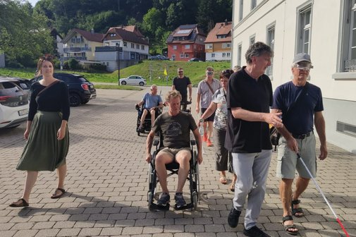 Die VdK-Ortsvorsitzende Verena Diemer schreitet neben dem im Rollstuhl sitzenden Stadtrat Klaus Eckert her, Stadtrat Bernhard "Pi" Steinebrunner mit Augenmaske und Blinden-/Langstock wird von Beisitzer Rüdiger Hasberg geführt.