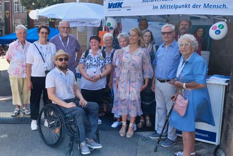 Gruppenbilder von 13 Personen vor einem Infostand mit VdK-Werbung. Unter der Gruppe Verena Bentele in einem Sommerkleid.