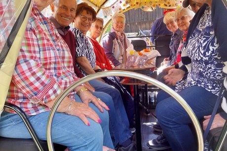 Rückblick in die Kutsche mit Sitzbänken rechts und links, die vollständig mit älteren Personen besetzt sind.