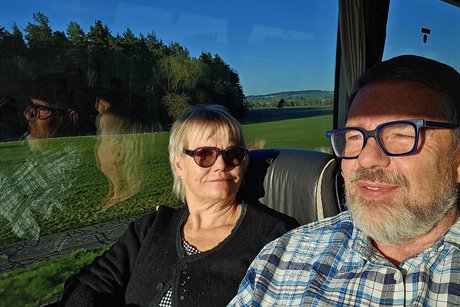 Der Vorsitzende im karierten Hemd sitzt zufrieden neben seiner Frau im Bus.