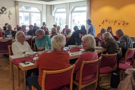 Panoramafoto des Festsaals mit mehreren Tischen, an denen vorwiegend &auml;ltere Menschen sitzen und sich angeregt unterhalten