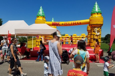 Hüpfburg im Hintergrund, davor stehen Eltern mit ihren Kindern.