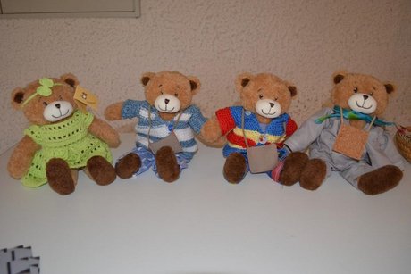 Vier Teddybären in bunter, selbst gestrickter Kleidung.