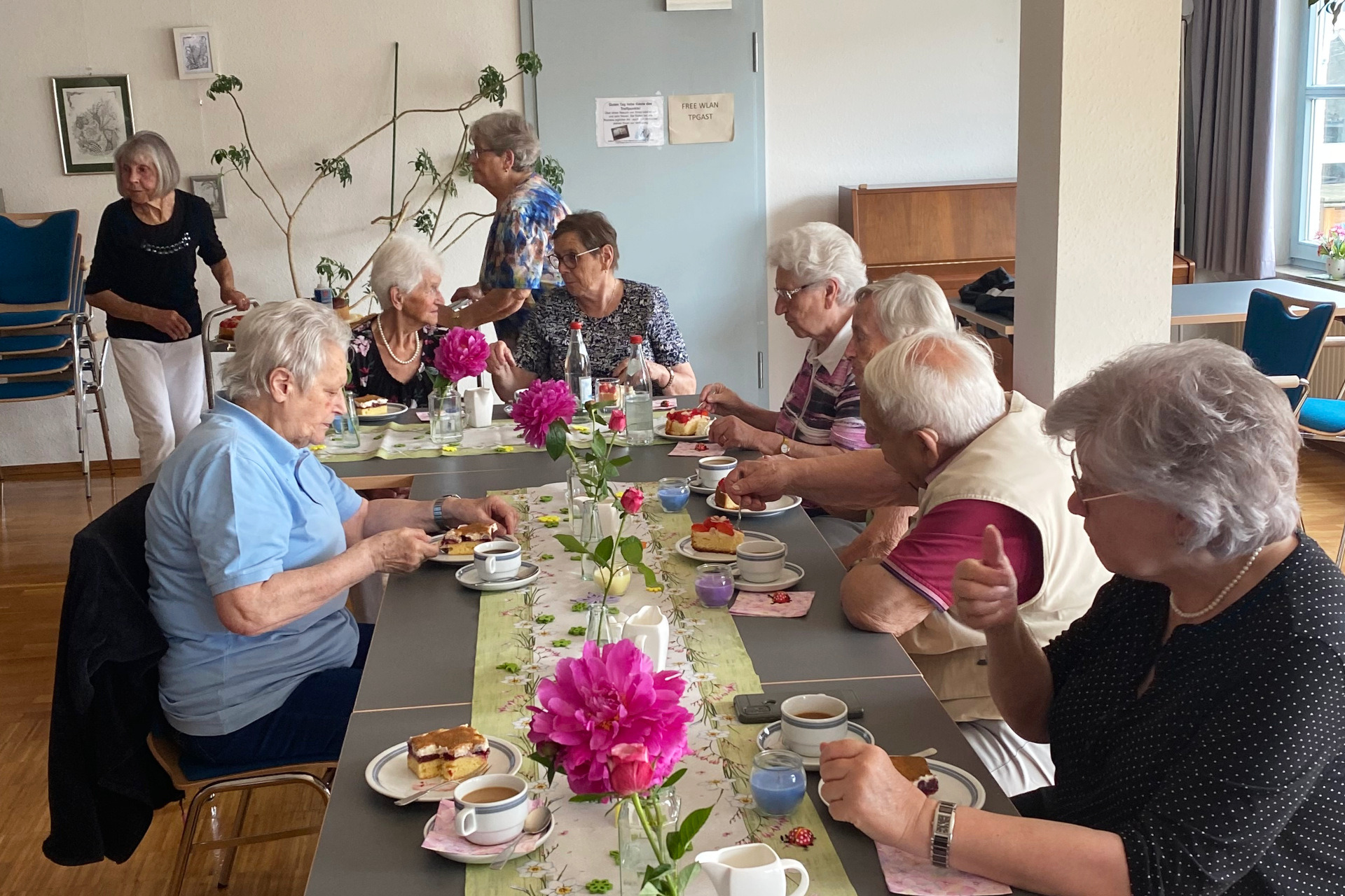 Frühlingsfest Sieben ältere Männer und Frauen sitzen gemeinsam an einem Tisch, essen Kuchen und unterhalten sich angeregt.