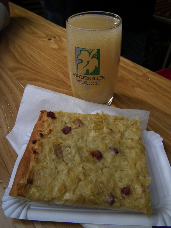 Das Bild zeigt ein Stück Zwiebelkuchen mit einem Glas neuem Wein