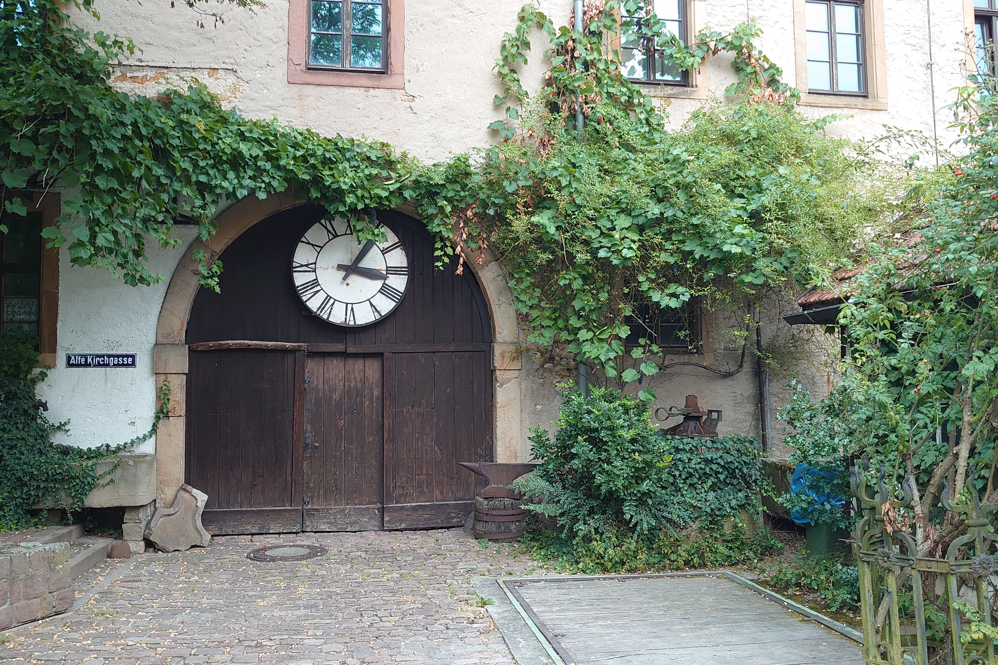 altes Scheunentor mit gro&szlig;en Uhrenzifferblatt umrankt von Efeu im Hof des Winzermuseums Rauenbergg