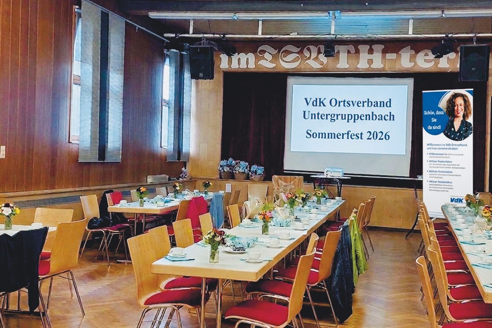 Saal mit geschm&uuml;ckten Tischreihen. Hintergrund B&uuml;hne mit gro&szlig;er Leinwand. Text: VdK Ortsverband Untergruppenbach Sommerfest 2026