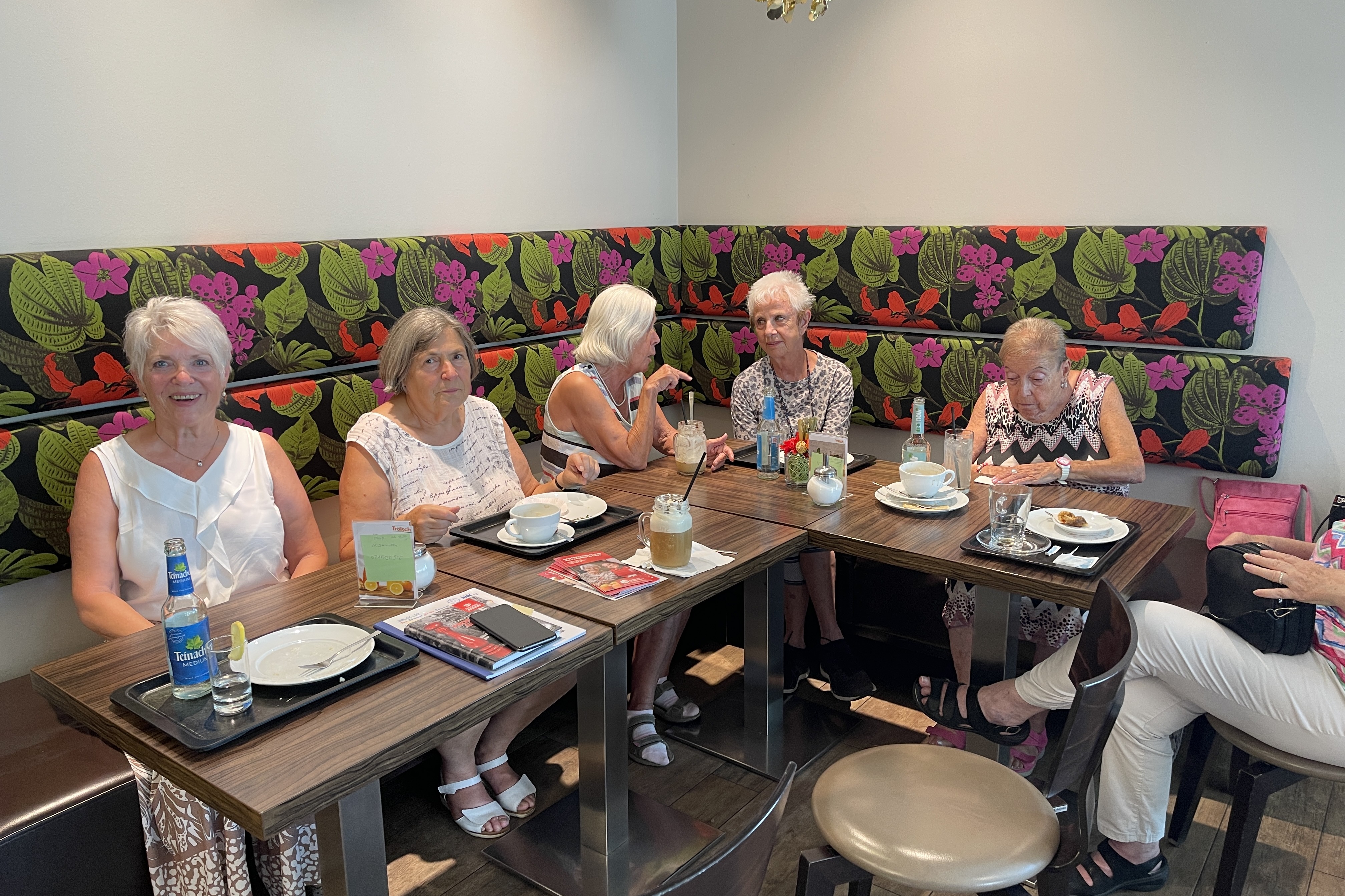 Es sitzen ein paar Leute bei Kaffee und Kuchen an einem Tisch und unterhalten sich.