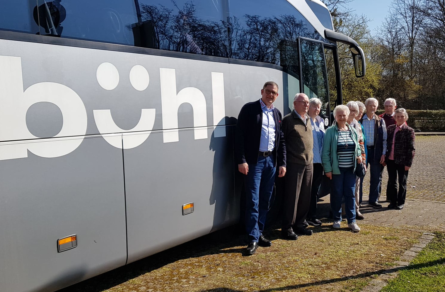 Reisegruppe älterer Menschen steht vor einem Reisebus.