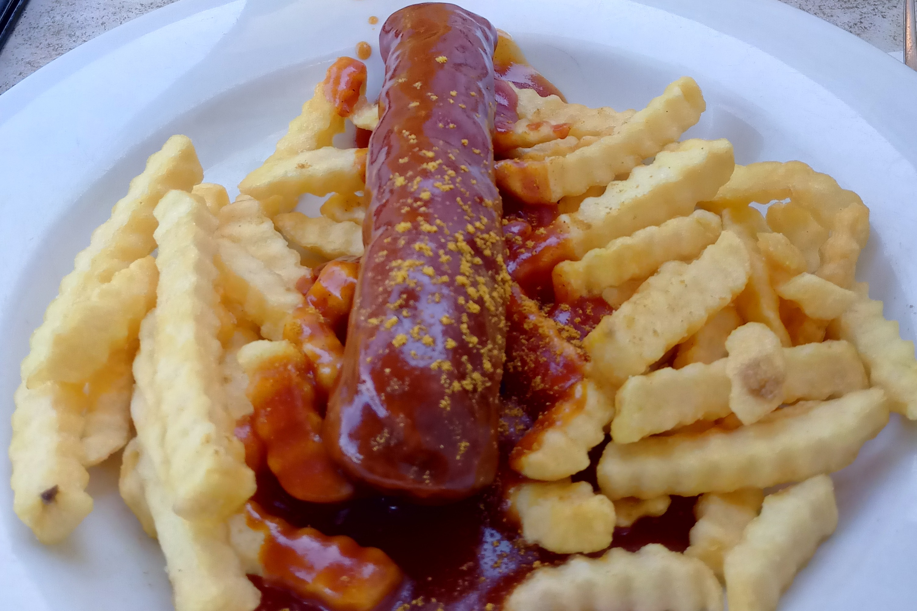 Das Bild zeigt eine Currywurst mit Pommes