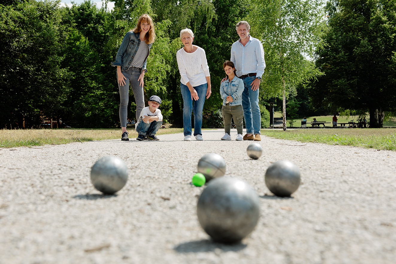 Boule spielende Menschen im Hintergrund (vier Erwachsene, ein Kind), gespielte Boule-Kugeln im Vordergrund.