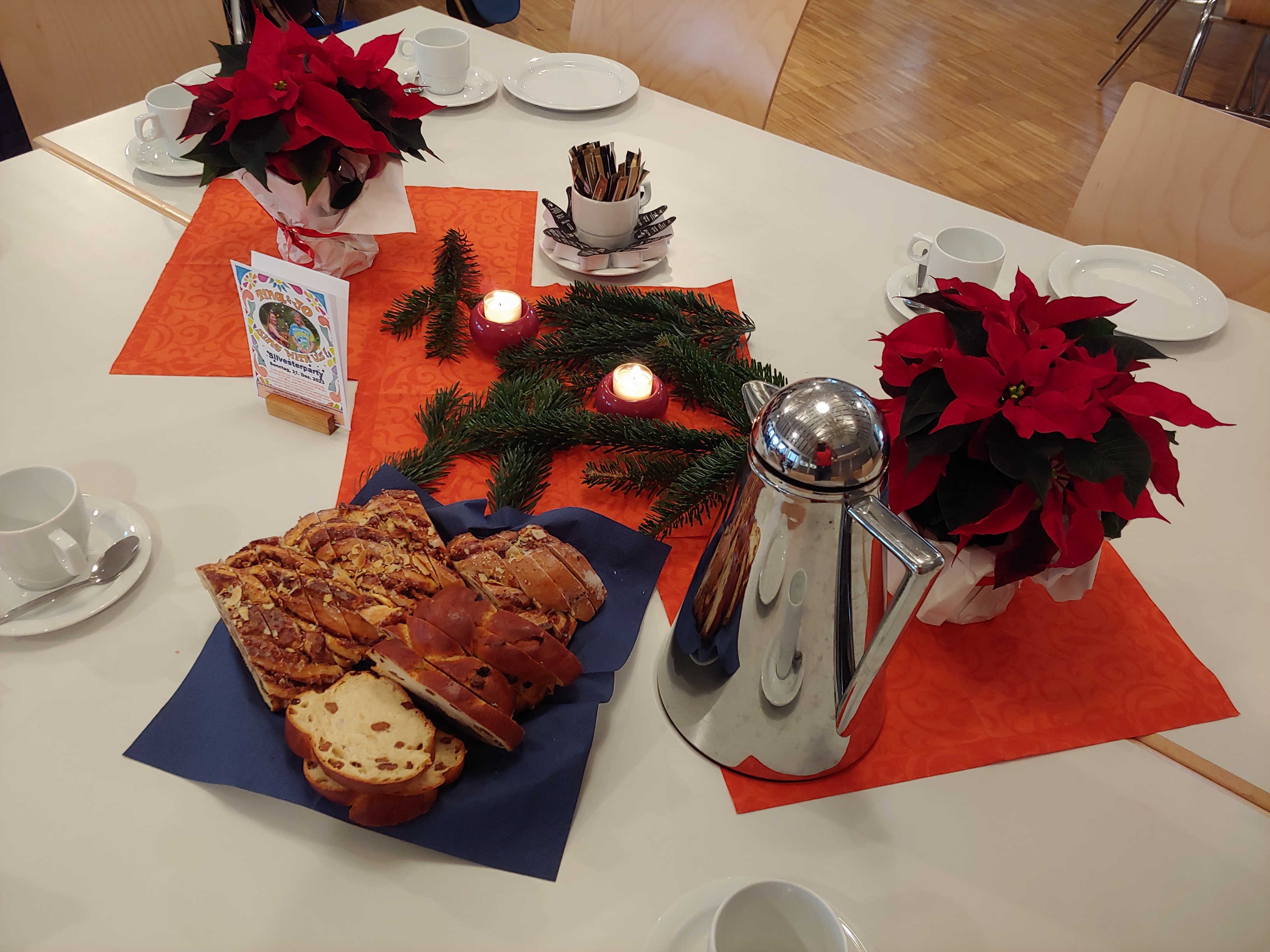 Gedeckter Tisch mit Kerzen, Geschirr, Rosinenzopf und Weihnachtsstern