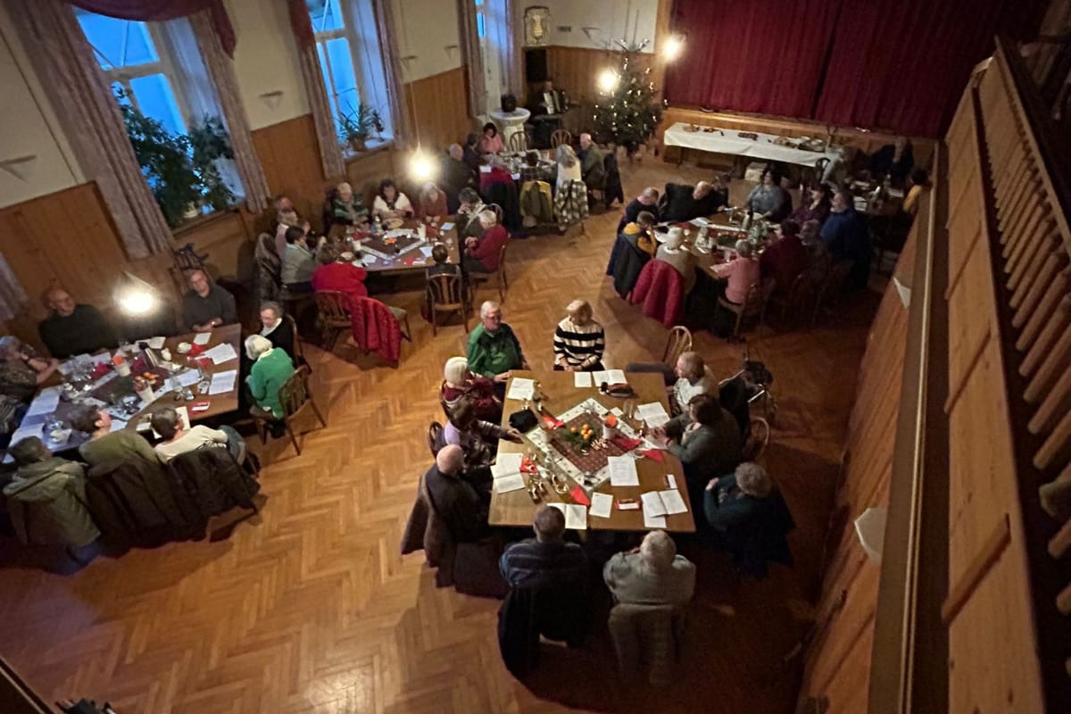 Ein Bild welches von der Empore aufgenommen wurde. Darauf sind 5 Doppeltische mit Personen zu sehen, welche gerade einige Weinachtslieder singen.