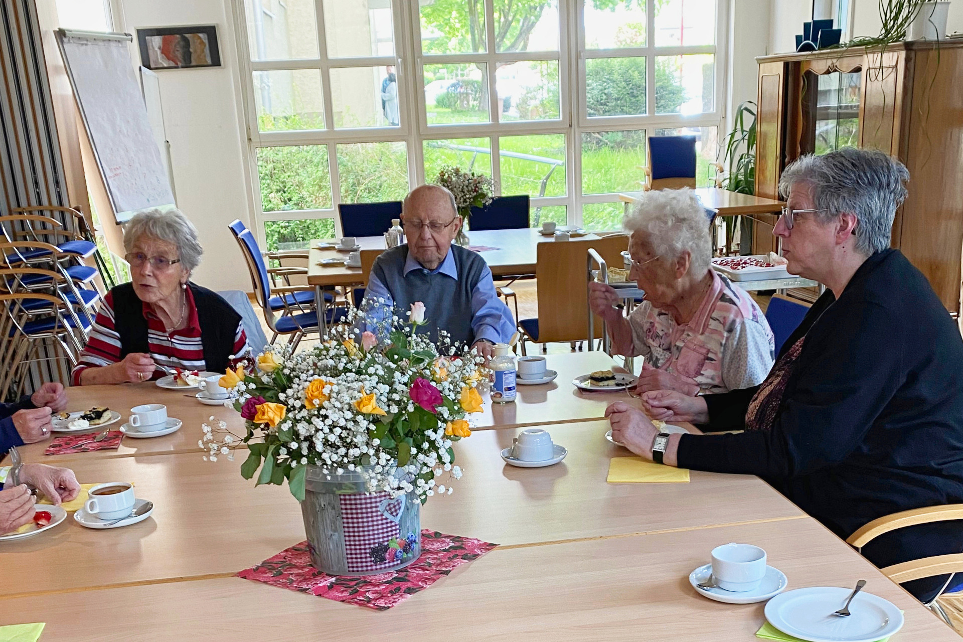 Kaffeenachmittag Drei Damen und ein Herr sitzen bei Kaffee und Kuchen an einem Tisch und unterhalten sich angeregt; in der Mitte des Tisches steht ein prächtiger Blumenstrauß.