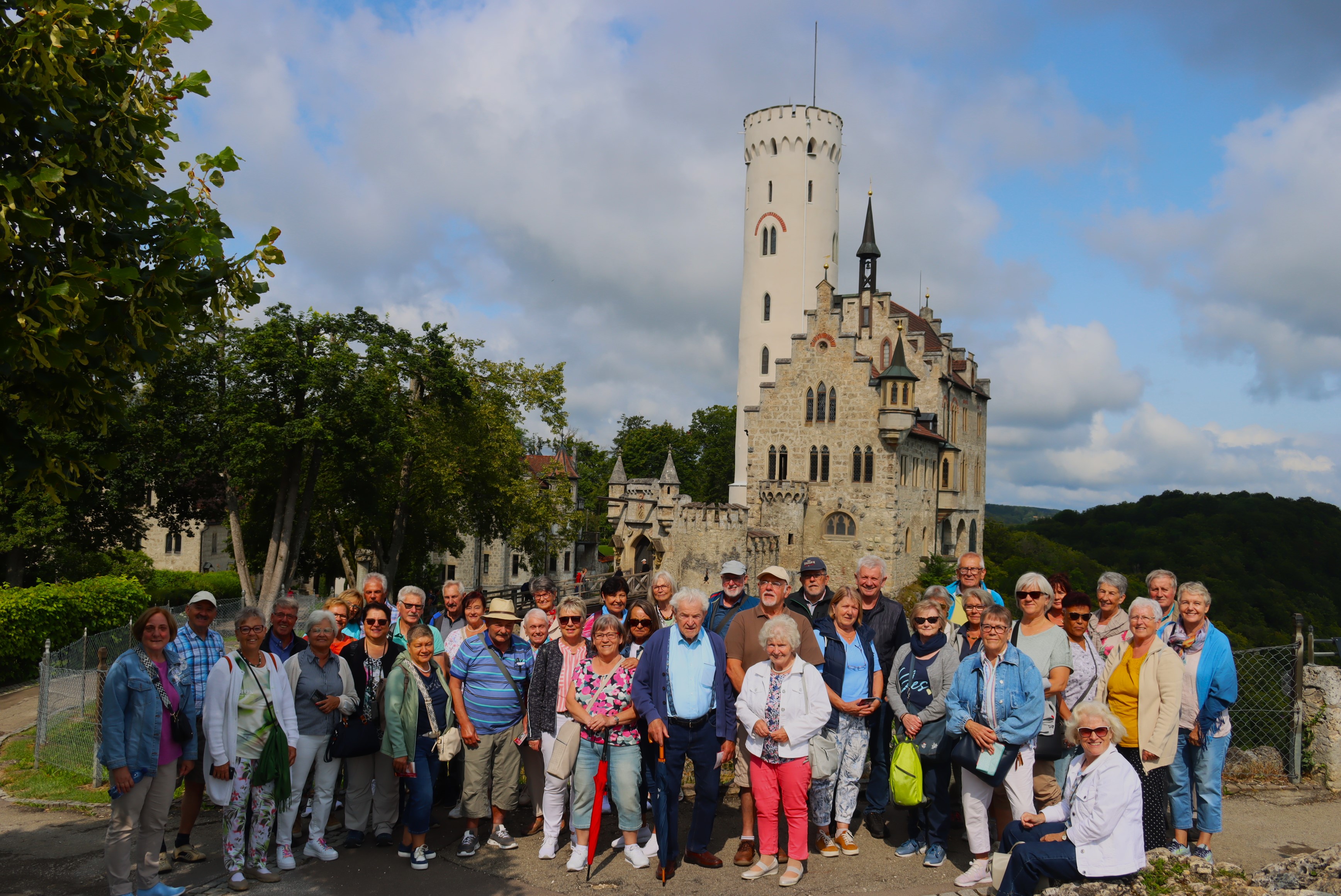 Reisegruppe steht vor dem Schloss Lichtenstein bei leicht bewölktem Himmer