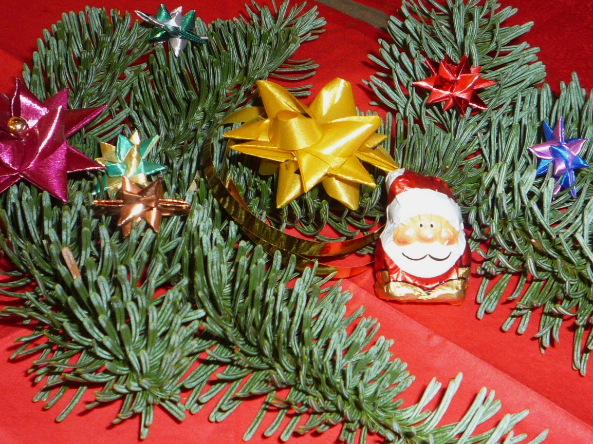 Zwischen Tannenzweigen ein kleiner Schokoladen-Nikolaus. Darum herum gebastelte Weihnachtssterne.