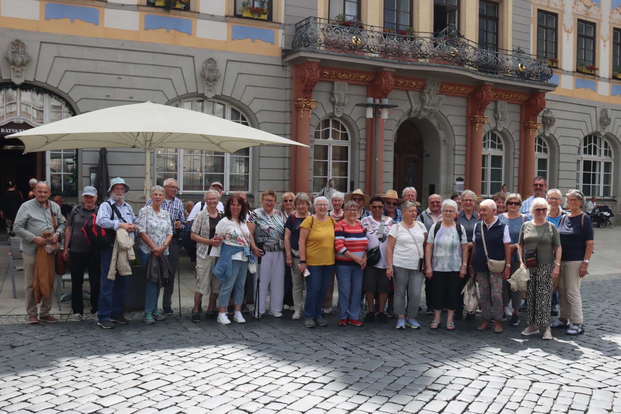 Reiseteilnehmer stehen vor dem Rathaus in Coburg, Vor dem Eingang stehen 4 rote S&auml;ulen, die einen Balkon mit schmiedeeisernem Ornamentegel&auml;nder tragenmitn S&auml;ulen