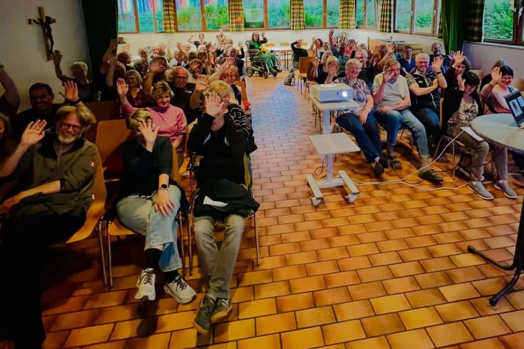 Impression vom Vortrag des SKM Lörrach Der Pfarrsaal aus der Perspektive der Vortragenden, 60 Menschen winken freundlich in die Kamera.