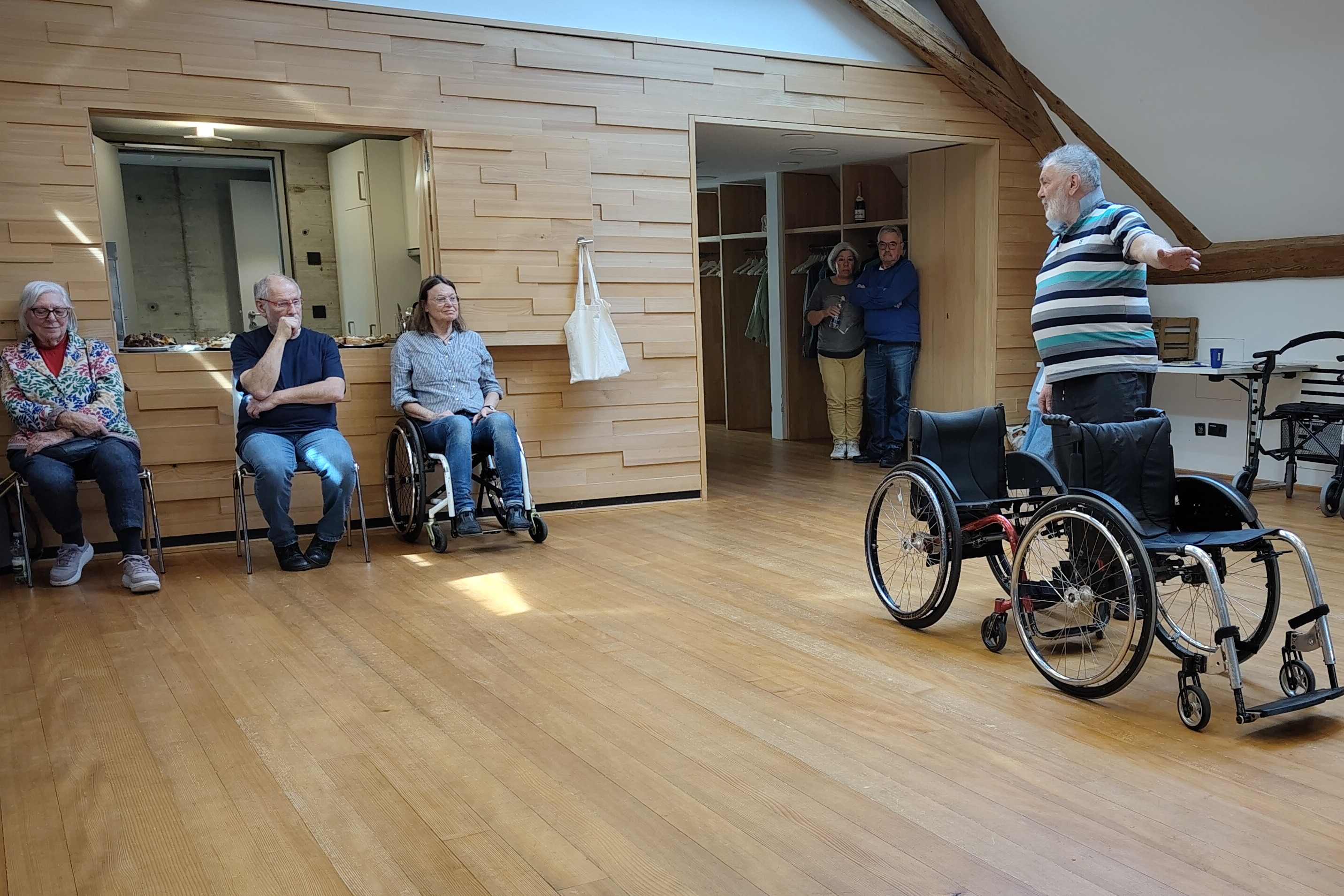 Rechts: Inklusionsp&auml;dagoge Holger Kranz erl&auml;utert anhand zweier mechanischer Rollst&uuml;hle die Rollstuhlarten, die Zuh&ouml;rern sitzen am Rand des B&uuml;rgersaals