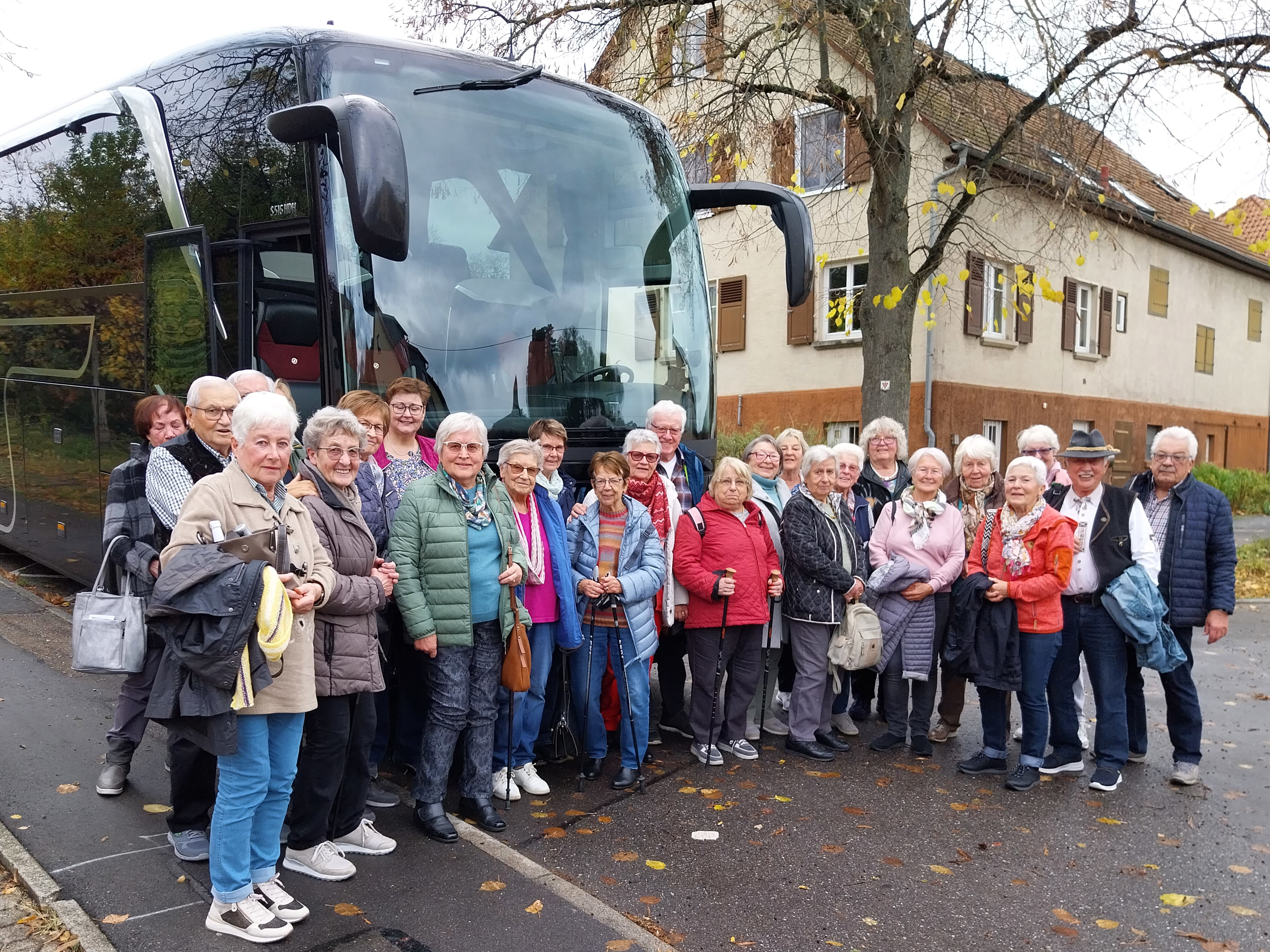 Reisegruppe älterer Menschen steht vor einem Reisebus.