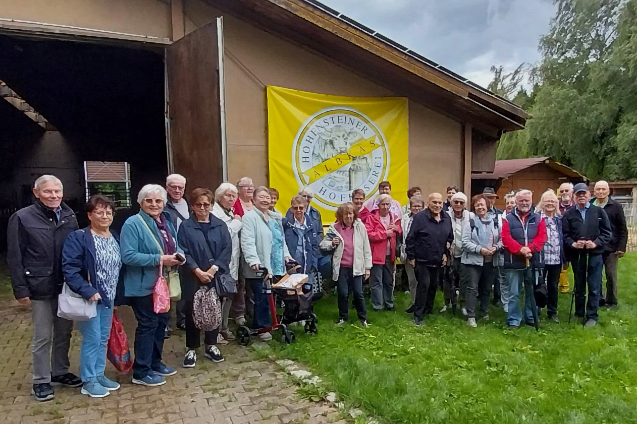 Sommerausflug VdK OV RSKN-Esslingen 2025 Ältere Menschen vor einer Scheune mit einem Plakat der Hohensteiner Hofkäserei Albkäs
